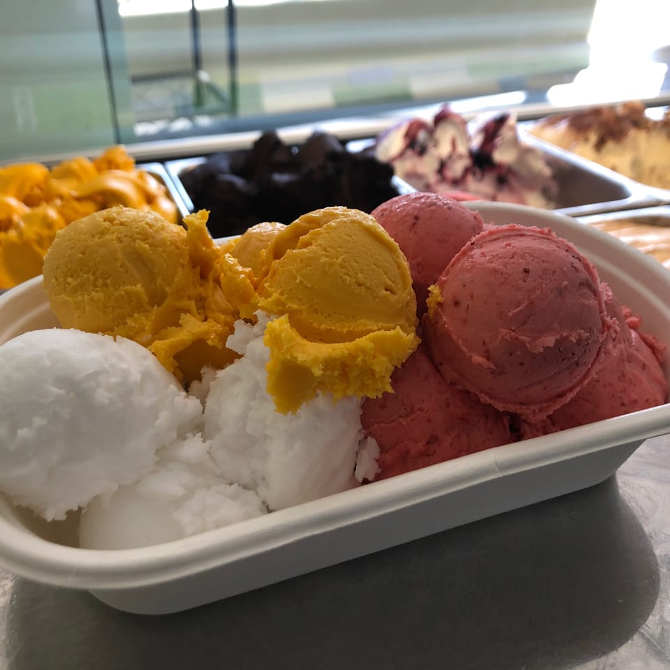 A white container filled with scoops of white, yellow, and pink gelato, with more flavors in the background.